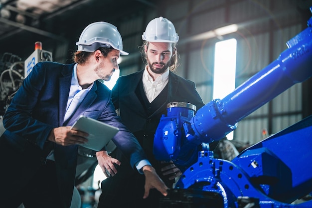 Foto los ingenieros de negocios se reúnen y controlan el brazo del robot de la máquina pesada equipo diverso de ingenieros de robótica industrial reunidos alrededor de la máquina operador de maquinaria profesional uso de tableta digital industrial