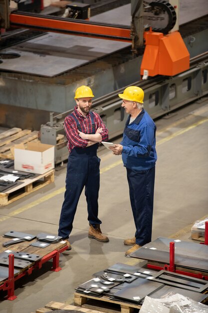 Ingenieros o técnicos jóvenes y superiores con cascos protectores y uniformes de pie dentro de la sala de almacenamiento y consultoría