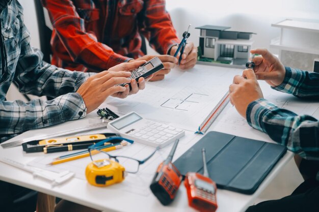 Ingenieros que se reúnen trabajando y señalando dibujos en la oficina para discutir herramientas de ingeniería y concepto de construcción