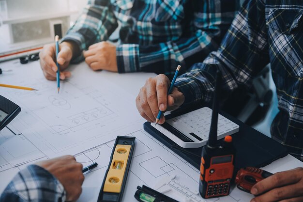 Ingenieros que se reúnen trabajando y señalando dibujos en la oficina para discutir herramientas de ingeniería y concepto de construcción