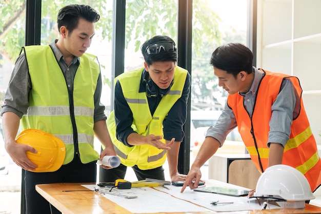 Ingenieros reunidos trabajando y señalando un plano en la oficina para discutir herramientas de ingeniería y concepto de construcción