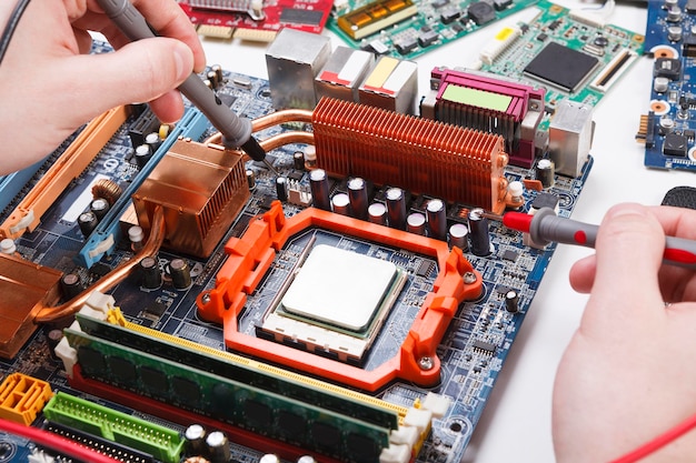 Ingenieur, der das Motherboard mit Multimeter-Nahaufnahme überprüft. Computerdiagnose, Wartungsunterstützung und Reparaturservicekonzept.