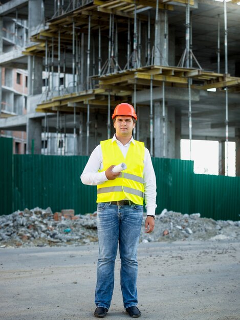 Ingenieur im Helm auf der Baustelle posiert gegen Gerüste