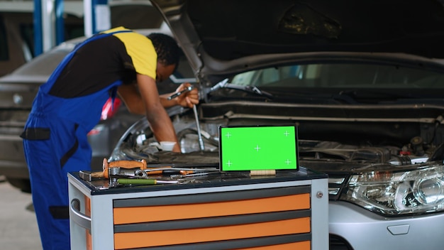 Ingenieur im Kfz-Service verwendet Drehmomentschlüssel, um Schrauben im Fahrzeug zu befestigen, mit grünem Bildschirm davor. Der Experte nutzt professionelle Werkzeuge, um neben dem Modellgerät ein defektes Auto zu reparieren