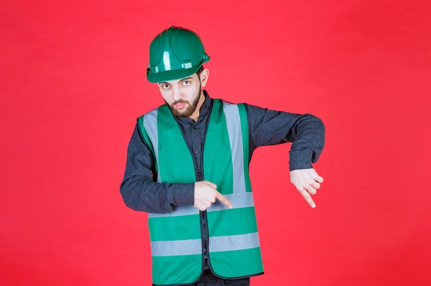 Ingenieur in grüner Uniform und Helm, der unten etwas zeigt.