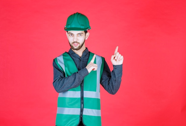 Ingenieur in grüner Uniform und Helm nach oben zeigend.