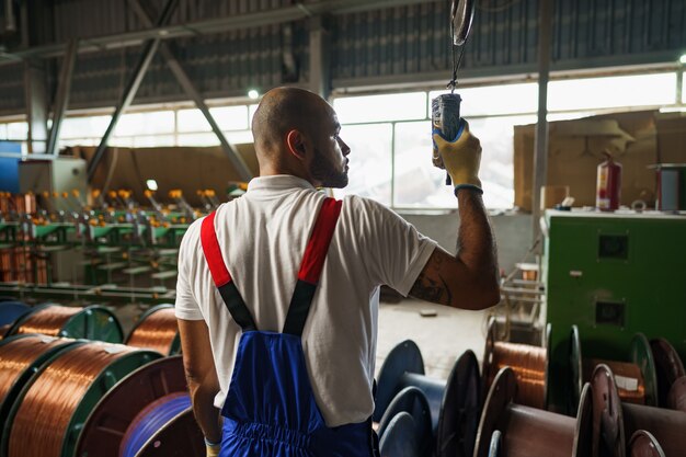 Ingenieur in Uniform mit von der Decke hängender Kransteuerung in einer Fabrik