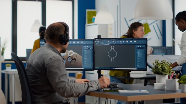 Ingenieur mit Headset arbeitet am PC-Bildschirm und zeigt CAD-Software mit d-Konstruktionsmetallkomponenten ...