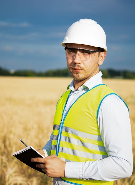 Ingenieur mit Helm, Schutzbrille und gelber Weste, eine Hand am Helm mit einem Notizblock, einem Ordner