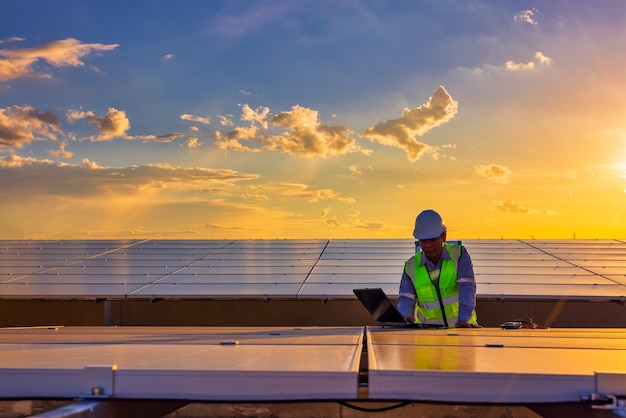 Ingenieur mit Laptop an Sonnenkollektoren auf dem Dach bei Sonnenuntergang Himmel Ingenieur arbeitet an einer Photovoltaik