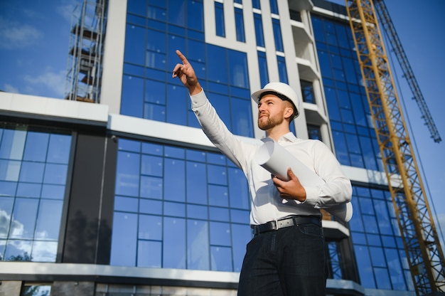 Ingenieur neben Baukränen. Konzept - großes Bauprojekt. Architekt leitet den Bauprozess. Zeichnungen und Tablet in den Händen.