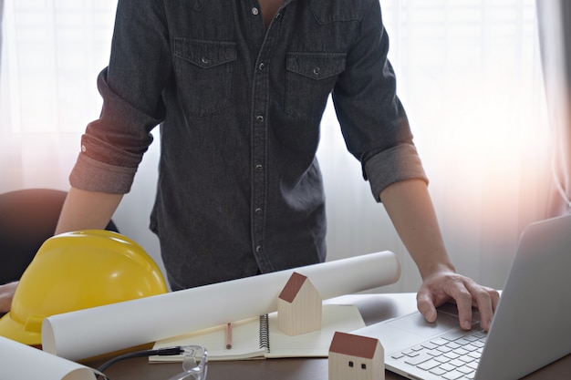 Ingenieur oder Architekt, der Computer-Laptop für Konstruktionsentwurf mit dem Bauplan auf dem Schreibtisch im Büro verwendet.