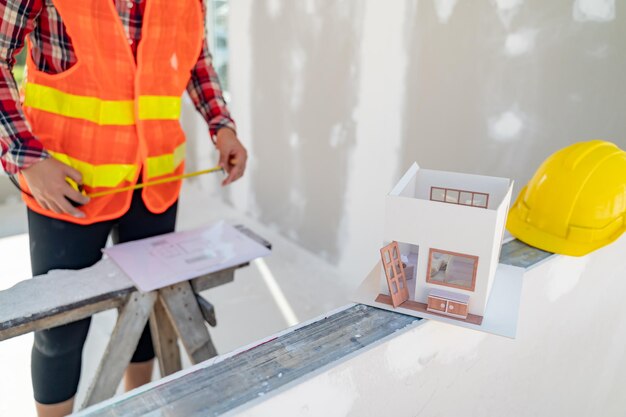 Ingenieur- und Architektenfrau, die mit Hausmodell auf der Baustelle arbeitet.