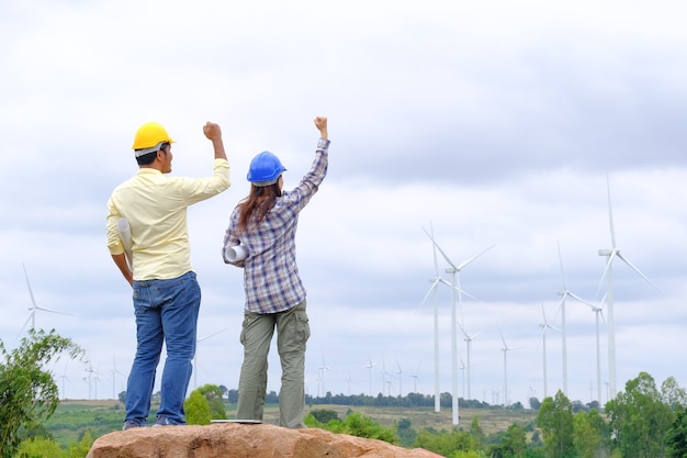 Ingenieure stehen mit Blaupausen und gratulieren Windturbinenprojekten zur Stromerzeugung und zur Überprüfung der Windrichtung.