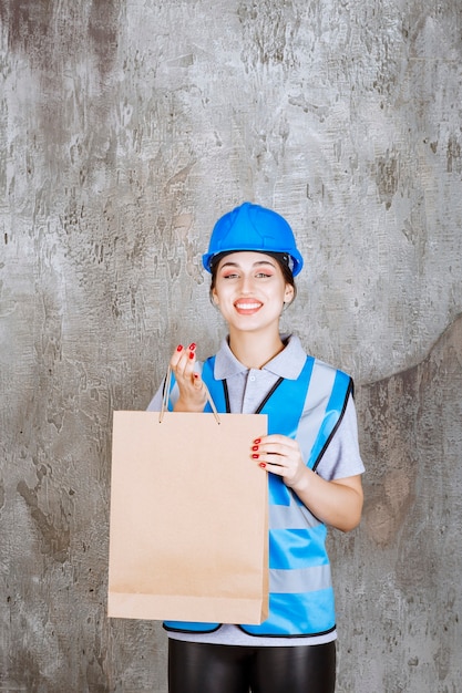 Ingenieurin in blauer Uniform und Helm, die eine Einkaufstasche hält und überrascht aussieht.