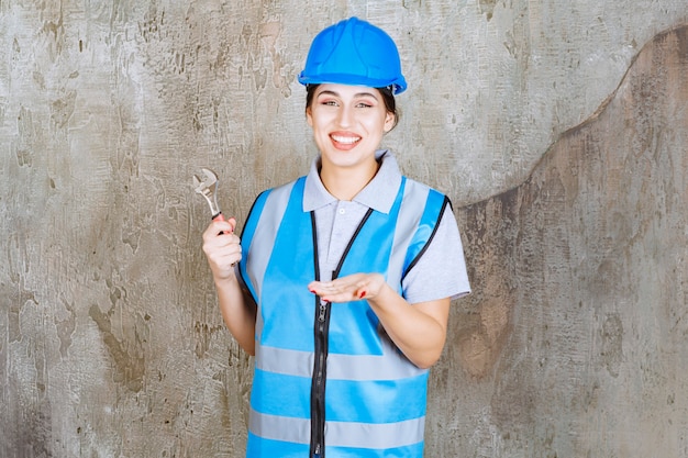 Ingenieurin in blauer Uniform und Helm hält einen Metallschlüssel.