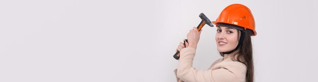 Ingenieurin in einem orangefarbenen Bauhelm mit einem Hammer auf weißem Hintergrund