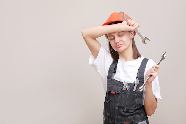 Ingenieurin in grauer Uniform und Schutzhelm lächelt mit Werkzeugen und Schraubenschlüsseln in den Händen.