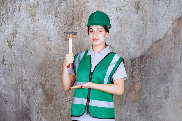 Ingenieurin mit grünem Helm, die eine Holzaxt für Reparaturarbeiten hält