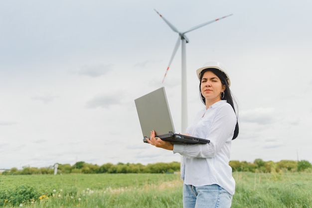 Ingenieurin mit Schutzhelm bei der Windkraftanlage, die am Laptop arbeitet