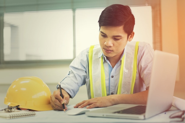 Ingenieurmann, der mit dem Laptop und Plänen ein Bauprojekt skizzieren arbeitet