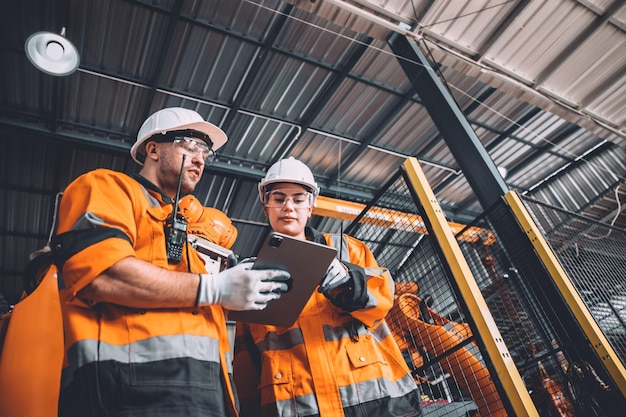 Ingenieurteam Serviceroboterschweißen, das in der Automatisierungsfabrik arbeitet Mitarbeiter in Sicherheitsanzügen arbeiten an der Softwareprogrammierung des Roboterarms oder ersetzen Teile in der Technologie der automatisierten Fertigungsindustrie