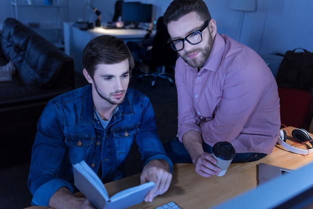 Ingenieurtechnik. Ernsthafte positive gutaussehende Männer, die vor dem Computerbildschirm sitzen und sich auf ihr Projekt konzentrieren, während sie im Büro arbeiten