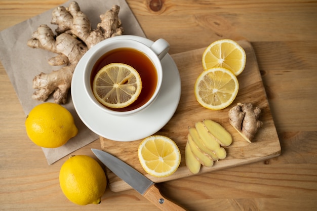 Foto ingrediente para calentar el té. raíces de jengibre enteras y en rodajas, limón en la vista superior de la pared blanca.