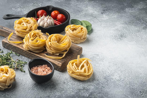 Ingrediente da cozinha mediterrânea tradicional conjunto de tagliatelle de massa não cozida, em mesa de pedra cinza