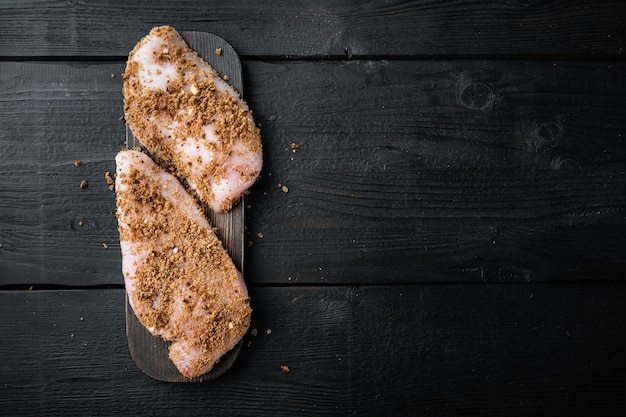 Ingrediente de peitos de frango crus esfarelados, em fundo preto de madeira, plano com espaço para texto