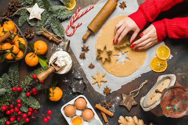 Ingredientes alimentares de férias para fazer pequenas árvores de biscoitos de gengibre de Natal e mão de mulher de floco de neve com ...