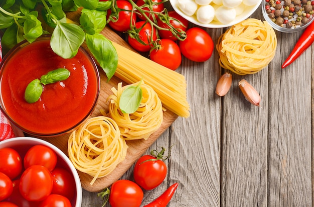 Ingredientes alimentarios italianos mozzarella, tomate, albahaca y aceite de oliva sobre fondo de madera rústica.