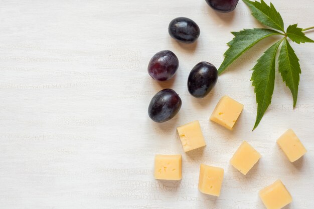 Ingredientes para aperitivos, queso con aceitunas sobre una mesa blanca.