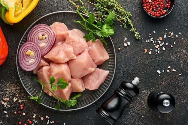 Ingredientes de carne de piezas crudas de pollo sobre tabla de madera, especias, hierbas y verduras sobre fondo gris oscuro. Ingredientes crudos para gulash o shish kebab. Vista superior. Espacio de copia gratuito.