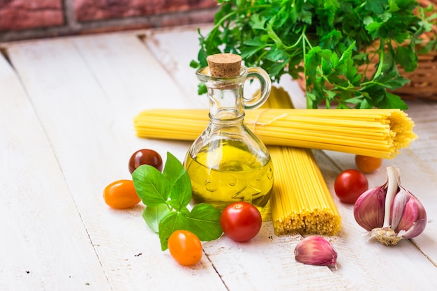 Ingredientes de la cena italiana en mesa de madera, espaguetis, aceite de oliva, tomates cherry, ajo, albahaca, perejil