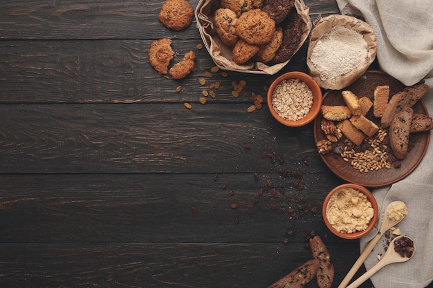 Ingredientes de cocina para galletas de avena caseras y biscotti. Copos de avena y harina en cuencos de madera de fondo rústico oscuro con espacio para copiar, vista superior. Maqueta de concepto y receta de pastelería hecha a mano