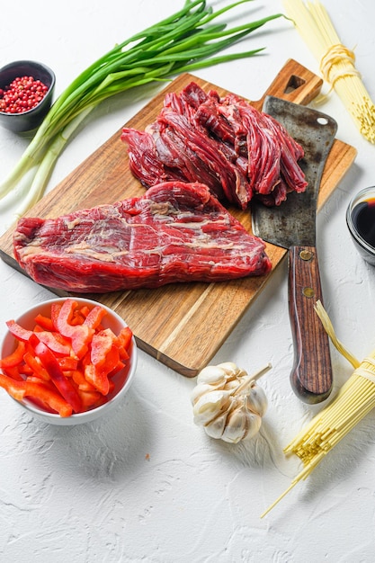 Ingredientes de cocina para hacer yakisoba salteado con carne de res. Vista lateral sobre una mesa de hormigón blanco.