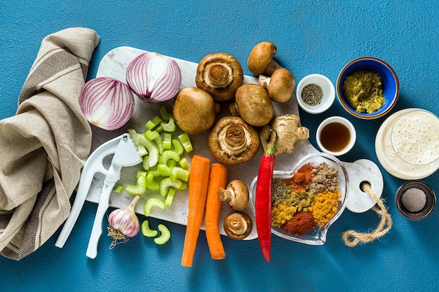 Ingredientes para cocinar curry indio a partir de verduras, calabazas y champiñones sobre un fondo azul y especias tomadas desde arriba del espacio de copia