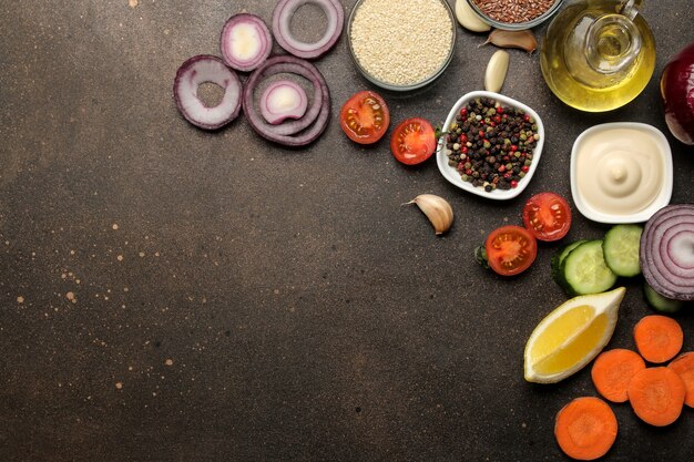 Foto ingredientes para cocinar ensalada. varias verduras y especias zanahorias, tomates, cebollas, pepinos, pimientos y rúcula sobre un fondo oscuro. vista superior.