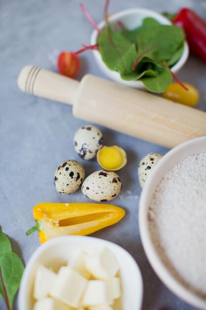 Ingredientes para cocinar vegetales Verduras frescas de colores huevos de codorniz mantequilla harina integral y rodillo sobre un fondo gris Fondo de panadería