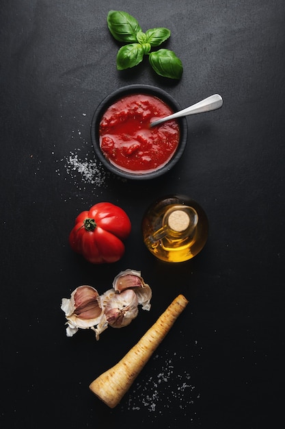 Ingredientes de la comida italiana con verduras y salsa de tomate en la mesa oscura. Vista superior.