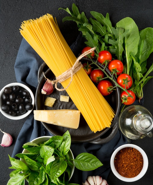Ingredientes crudos para cocinar espaguetis. Pasta, tomate, ajo, albahaca, parmesano y aceitunas.