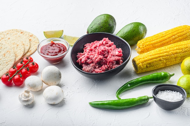 Ingredientes crus para tacos com carne picada de carne, tortilhas de milho, pimenta, abacate, sobre fundo branco