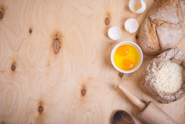 Ingredientes de panificação em fundo rústico com pão, casca de ovo, pão, farinha, rolo de massa