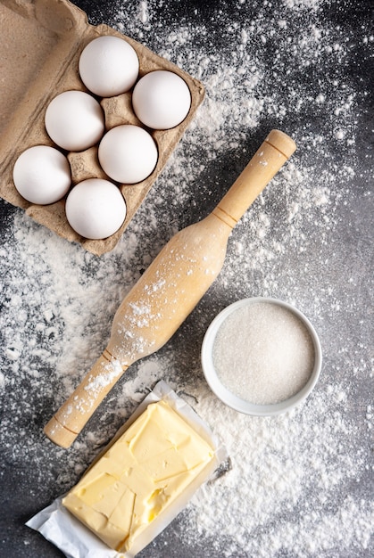 Ingredientes de panificação: farinha, ovos, manteiga e açúcar, com rolo em uma mesa