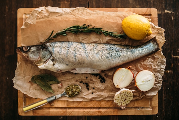 Ingredientes de preparação de peixe fresco, ervas, especiarias, cebola e alho, limão na tábua de cortar coberto com papel manteiga, vista superior