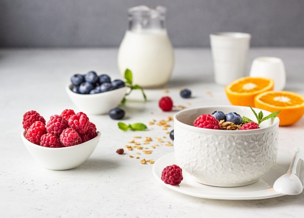 Ingredientes do café da manhã saudável. Tigela de granola caseira com leite, frutas frescas (mirtilo e framboesa), laranja e leite.