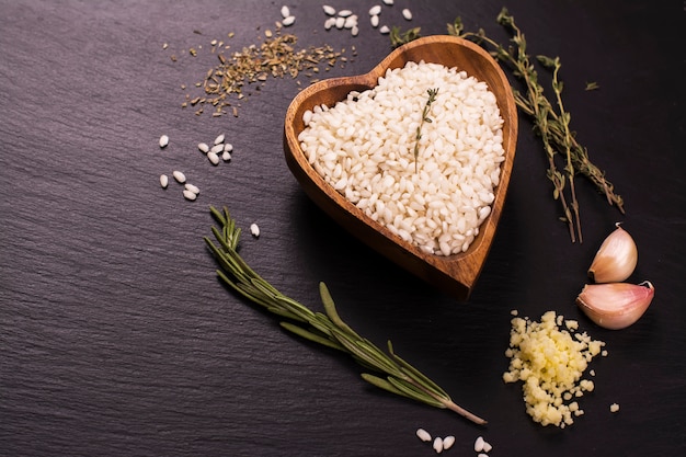 Ingredientes do Risotto no fundo de pedra preto: arroz, alho, parmesão e ervas