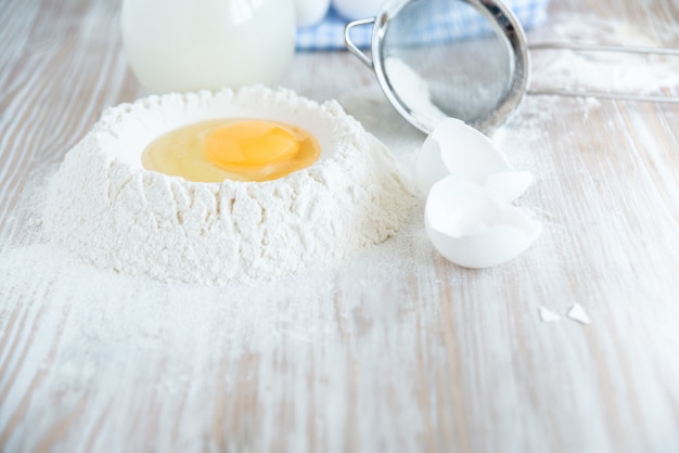 Ingredientes e utensílios para panificação - farinha, ovos e copo de leite na mesa rústica de madeira. preparação de massa caseira