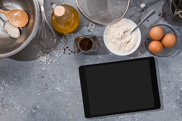 Ingredientes, ferramentas para panificação e tablet com tela em branco e local para texto ou imagem na mesa cinza. receita, livro de receitas, modelo online de cursos de culinária